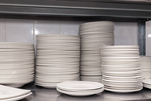 Montón de placas de porcelana blanca de cerámica limpia en un estante de metal en la parte posterior del restaurante. Concepto de preparación para un banquete, catering, buffet
 - Foto, Imagen