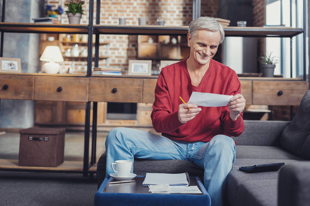 Cheerful pensioner smiling while looking at the bills in his hands - Photo, image