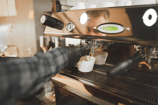 Yakın çekim fotoğraf bir barista'nın el bir tutucu elinde tutar ve bir profesyonel kahve makinesi kahve pişirmek. Bir barista kahve makinesi arka plan üzerinde elinde Portafilter. - Fotoğraf, Görsel