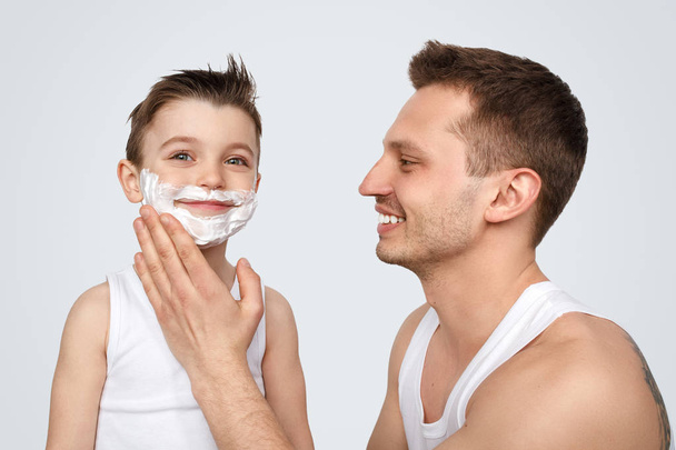 Cheerful father smearing shaving foam on son - Fotó, kép