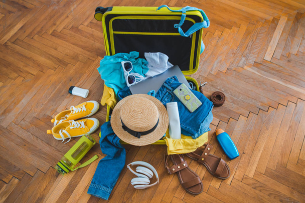 Reisekonzept. gelber Koffer mit verschiedenen Sachen drumherum. Ansicht von oben - Foto, Bild