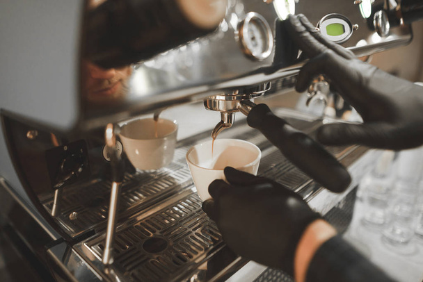 Close-Up photo egy professzionális kávéfőző főzés kávé, kávé öntenek egy csésze, a barista szabályozza a folyamatot. Barista-kesztyű készít egy illatos espresso egy étteremben, - Fotó, kép