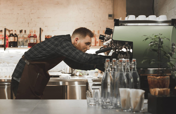 Il ritratto di un barista barbuto pulisce una macchina da caffè professionale dopo la cottura. Il barista sta preparando la macchina del caffè al caffè
. - Foto, immagini