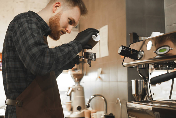 Владелец кофейни наливает кофе в портафилер у кофеварки. Бородатый бариста держит держатель в кафе и варки кофе
. - Фото, изображение
