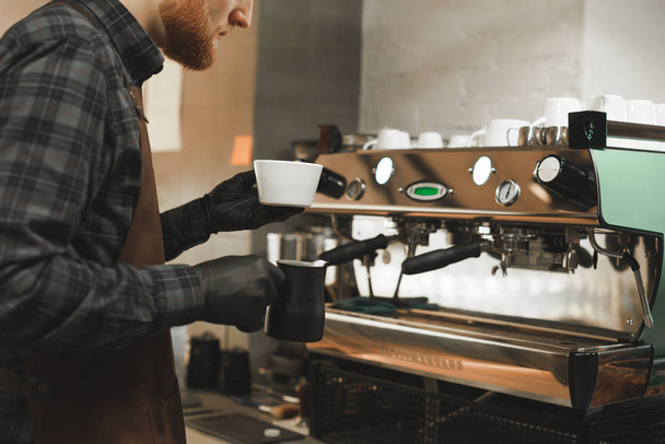 Parrakas barista tekee cappuccinoa kahvinkeittimessä. Lähikuva kuva kahvilan omistaja valmistaa kahvia juomaa. Kahvi käsite
. - Valokuva, kuva