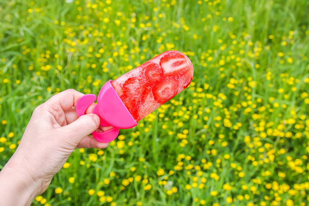 Hand holding strawberry ice cream cone on summer nature background in warm sunny day. Homemade fresh fruit dessert. - Photo, Image