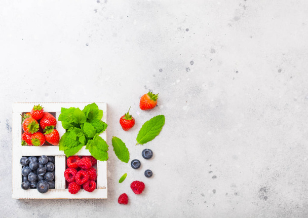 Fresh raw organic berries in white wintage wooden box on kitchen table background. Space for text. Strawberry, Raspberry, Blueberry and Mint leaf - Foto, Imagem