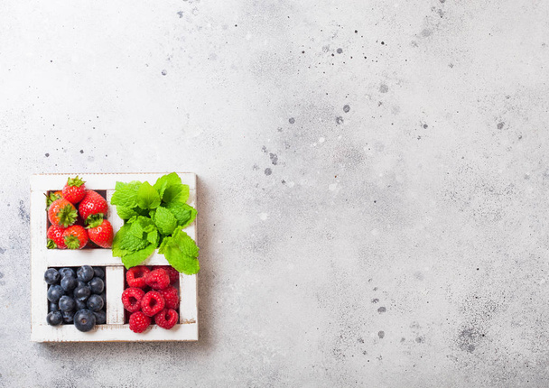 Fresh raw organic berries in white wintage wooden box on kitchen table background. Space for text. Strawberry, Raspberry, Blueberry and Mint leaf - Foto, immagini