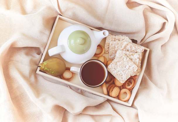 Café da manhã na cama em uma bandeja de madeira com pêra, biscoitos, biscoitos doces, bule e xícara de chá
. - Foto, Imagem