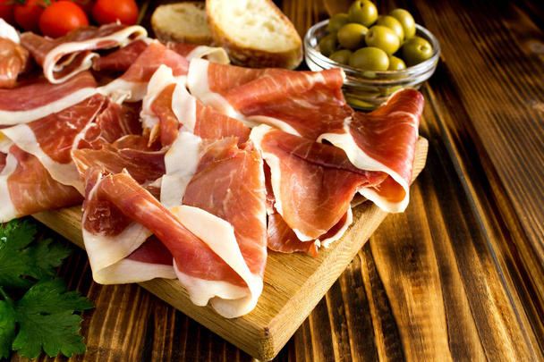 Spanish jamon  in the cutting board on the  brown  wooden background - Foto, afbeelding