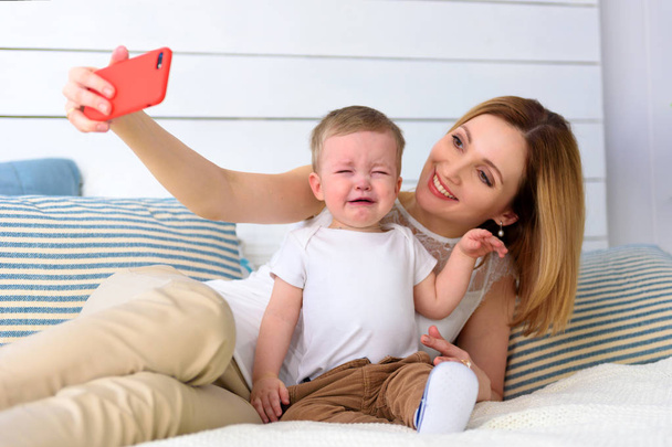 Μητέρα με κραυγή παιδί μωρό αγόρι photoshooting στο κόκκινο smartphone selfie στην αρχική αίθουσα. - Φωτογραφία, εικόνα