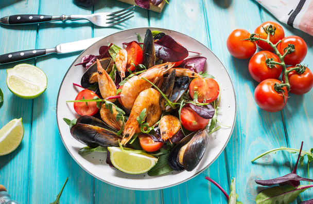 Fresh seafood salad, mussels, shrimp, fresh vegetables and herbs on blue wooden table. - Photo, Image