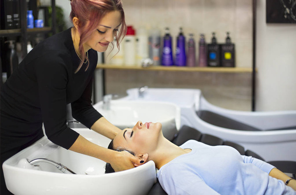 Linda jovem alegre desfrutando de massagem na cabeça enquanto recebe seu cabelo lavado por um cabeleireiro profissional. Cuidados de beleza, penteado, moda, estilo de vida conceito de glamour - Foto, Imagem