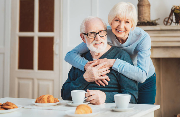 Cute couple of pensioners having warm croissants during breakfast - Foto, afbeelding