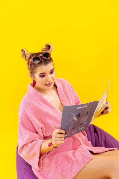 Young woman wearing pink bathrobe reading modern magazine - Fotografie, Obrázek