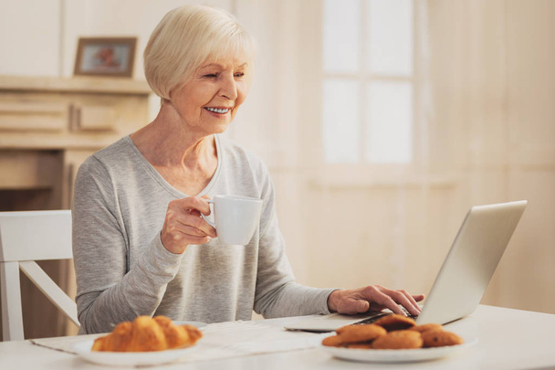 Pensioner smiling while watching family photos on laptop - Foto, Bild