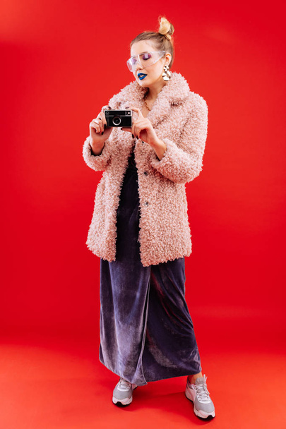 Slim woman wearing dress and pink coat holding photo camera - Foto, afbeelding