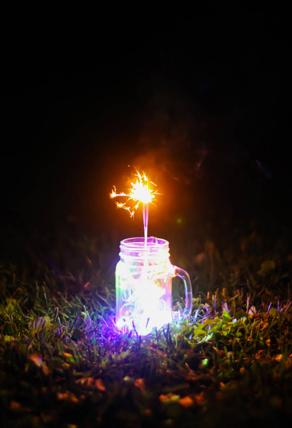 Juhlakortti, jossa kirkkaat värikkäät Garland-valot ja bengali-tulipalo lasipurkissa yön luontotaustalla. - Valokuva, kuva
