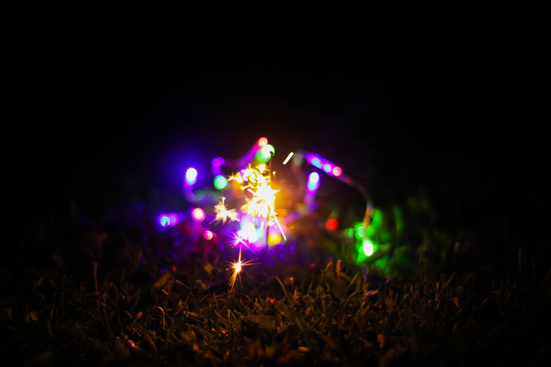 Juhlakortti, jossa kirkkaat värikkäät Garland-valot ja bengali-tulipalo lasipurkissa yön luontotaustalla. - Valokuva, kuva