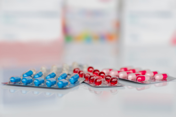 Medische pillen in wit, blauw, rood en andere kleuren. Pillen in plastic verpakking op witte spiegel achtergrond. Concept van gezondheidszorg en geneeskunde. - Foto, afbeelding