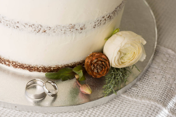 Closeup picture about a detail of white wedding cake with ornaments, with white gold wedding bands - Foto, Imagen