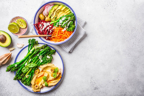 Vegan lunch concept. Rainbow vegetable salad and broccolini with hummus, top view. - Photo, image