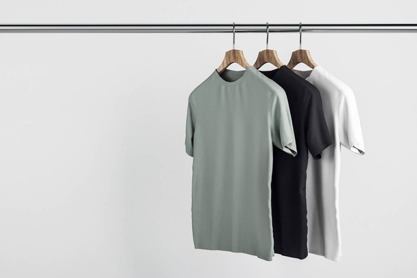 Empty grey, white and black tees on hanger. Concrete wall background. Design, store and style concept. Mock up, 3D Rendering  - Фото, зображення