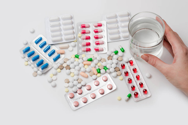 Un montón de medicamentos y pastillas con un vaso de agua en el fondo blanco. Vista superior
. - Foto, Imagen