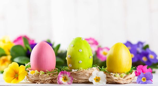Composición de Pascua con coloridos huevos de Pascua y flores de primavera sobre fondo de madera. Tarjeta de Pascua con espacio de copia
. - Foto, Imagen