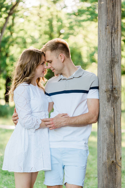 Young pretty couple in love standing in park. Handsome blonde girl in white dress hugging her boyfriend - Foto, Bild