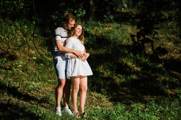 Young pretty couple in love standing in park. Handsome blonde girl in white dress hugging her boyfriend - Photo, image