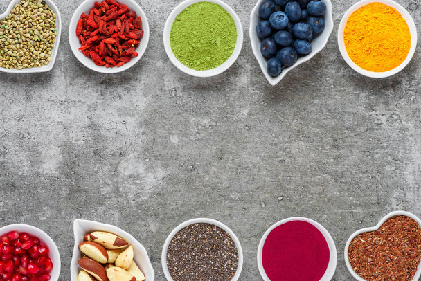 various superfoods on gray background. Superfood as chia, matcha, acai, turmeric, nuts, seeds, goji, blueberry. healthy vegan food concept. Top view with copy space - Photo, Image
