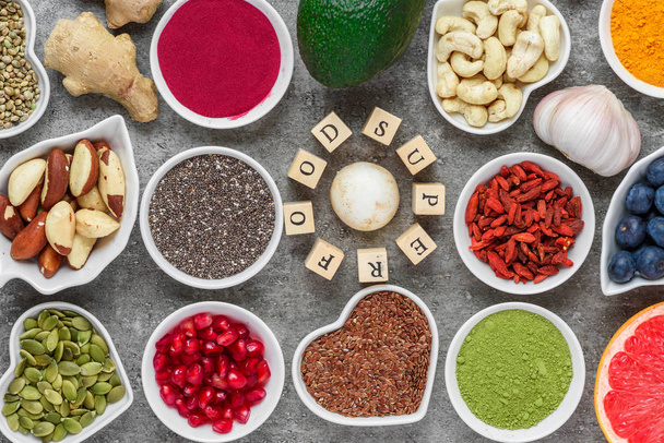 Superfood as acai, turmeric, matcha, seeds, blueberry, goji, ginger, grapefruit, mushrooms, pomegranate and nuts on dark concrete background vegan food concept top view - Photo, Image