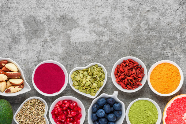 Auswahl an gesunden Lebensmitteln: Obst, Gemüse, Samen, Superfood, Nüsse, Beeren auf grauem Betonhintergrund. Ansicht von oben mit Kopierraum. Veganes Essen - Foto, Bild