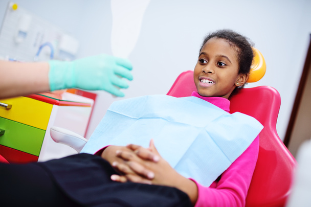 Afroamericana bambina sorridente seduta su una sedia dentale
 - Foto, immagini