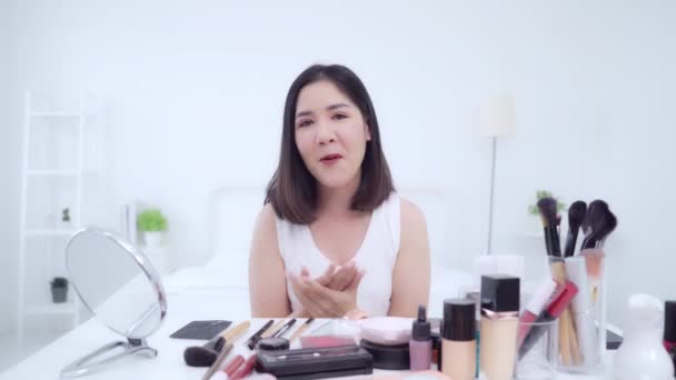 Beauty blogger present beauty cosmetics sitting in front camera for recording video. Happy beautiful young Asian woman use cosmetics review make up tutorial broadcast live video to social network. - Footage, Video