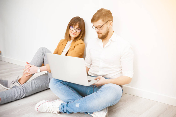 zwei junge Mitarbeiter lässig mit Laptop im weißen Interieur gekleidet - Foto, Bild