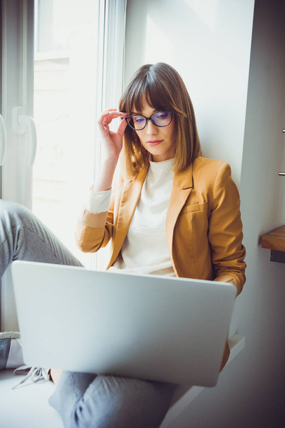 schöne Designerin Freiberuflerin mit Brille trägt lässig Laptop im weißen Büro - Foto, Bild