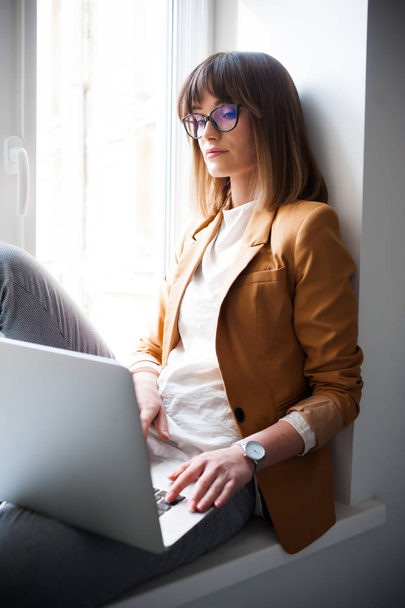 Belle femme designer pigiste dans les lunettes de vue porter occasionnel en utilisant un ordinateur portable dans le bureau blanc
 - Photo, image