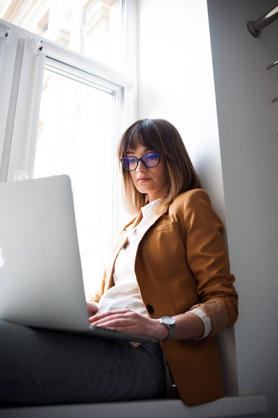 Beautiful woman designer freelancer in eyeglasses wearing casual using laptop in white office - Fotoğraf, Görsel
