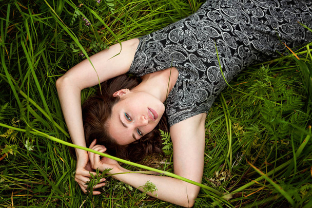 Brunette woman lying on green grass. Beauty Girl Outdoors enjoying nature and relaxation. Free Happy Woman. Top view - Zdjęcie, obraz