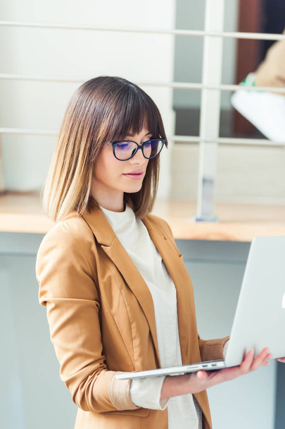Belle femme designer pigiste dans les lunettes de vue porter occasionnel en utilisant un ordinateur portable dans le bureau blanc
 - Photo, image