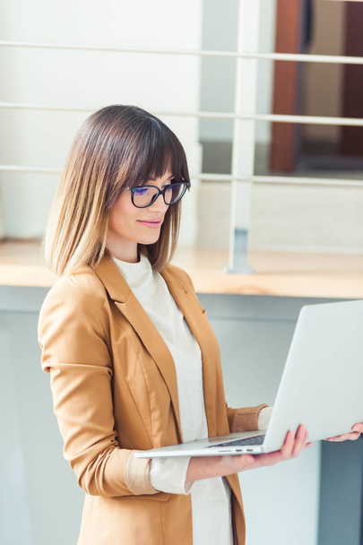 Красива жінка дизайнер фрілансер в окулярах носить повсякденне використання ноутбука в білому офісі
 - Фото, зображення