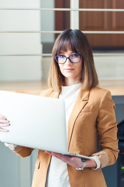 schöne Designerin Freiberuflerin mit Brille trägt lässig Laptop im weißen Büro - Foto, Bild