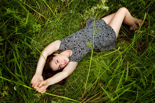 Μελαχρινή γυναίκα ξαπλωμένη στο πράσινο χορτάρι. Κορίτσι ομορφιά σε εξωτερικούς χώρους απολαμβάνοντας την φύση και χαλάρωση. Δωρεάν ευτυχισμένη γυναίκα. Το top view - Φωτογραφία, εικόνα