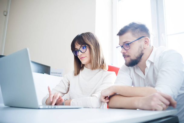 Két fiatal munkatársak öltözött alkalmi használ laptop-fehér belső - Fotó, kép