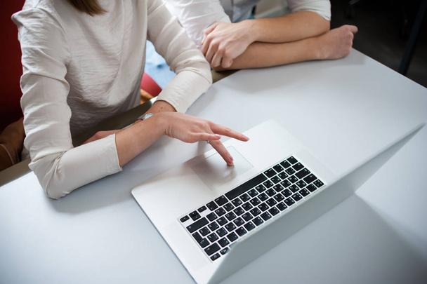Два молодых сотрудника одеты непринужденно, используя ноутбук в белом интерьере
 - Фото, изображение