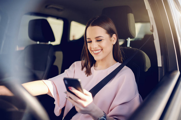 Portrait of gorgeous brunette with big toothy smile driving car and using smart phone. - Photo, Image
