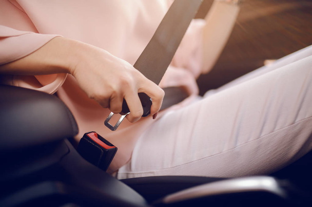 Close up of elegantly dressed Caucasian woman buckling seat belt while sitting in her car. - Foto, Bild