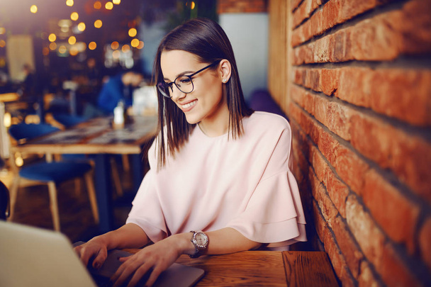 Morena atraente com óculos usando laptop enquanto sentado cafeteria pousada. No fundo efeito bokeh
. - Foto, Imagem